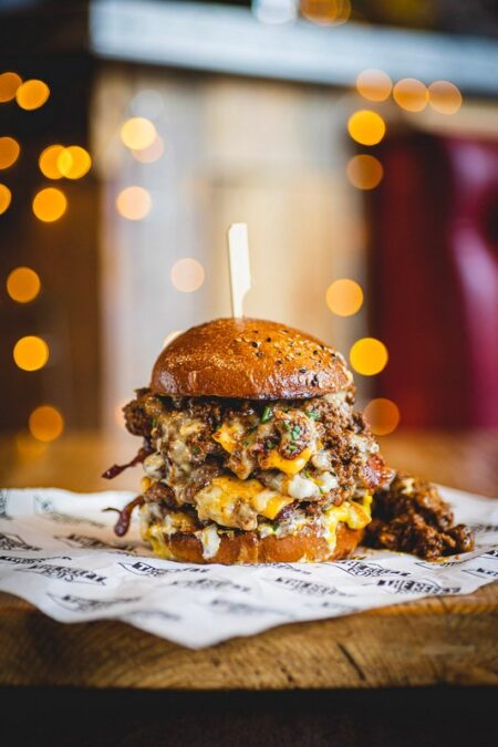 This monster burger features American cheese, Swiss cheese, crispy bacon, and a generous serving of spicy beef chilli. Topped with nacho cheese sauce, sour cream, Ball Park Mustard, pickled jalapeños, and chives