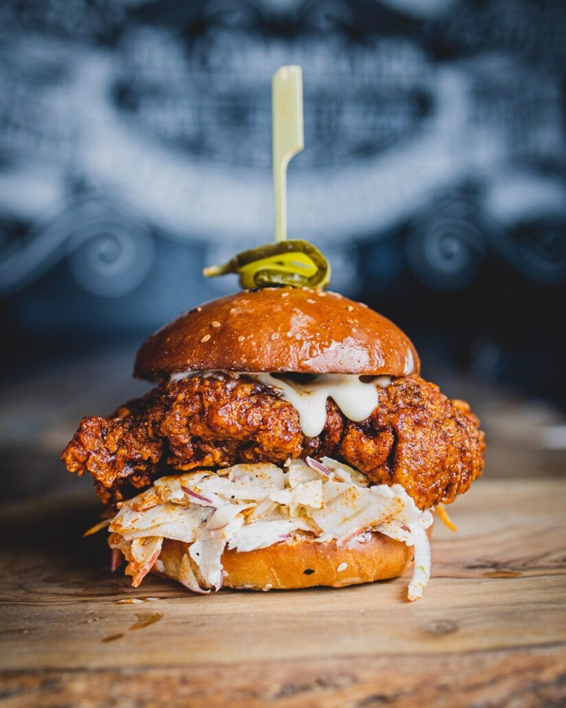 A ho0t n spicy Chicken Burger with Blue Cheese Mayo, Fennel, Apple & Blue Cheese Slaw, Gherkin on Top and Sprinkle of Tubby Toms Nashville Dust