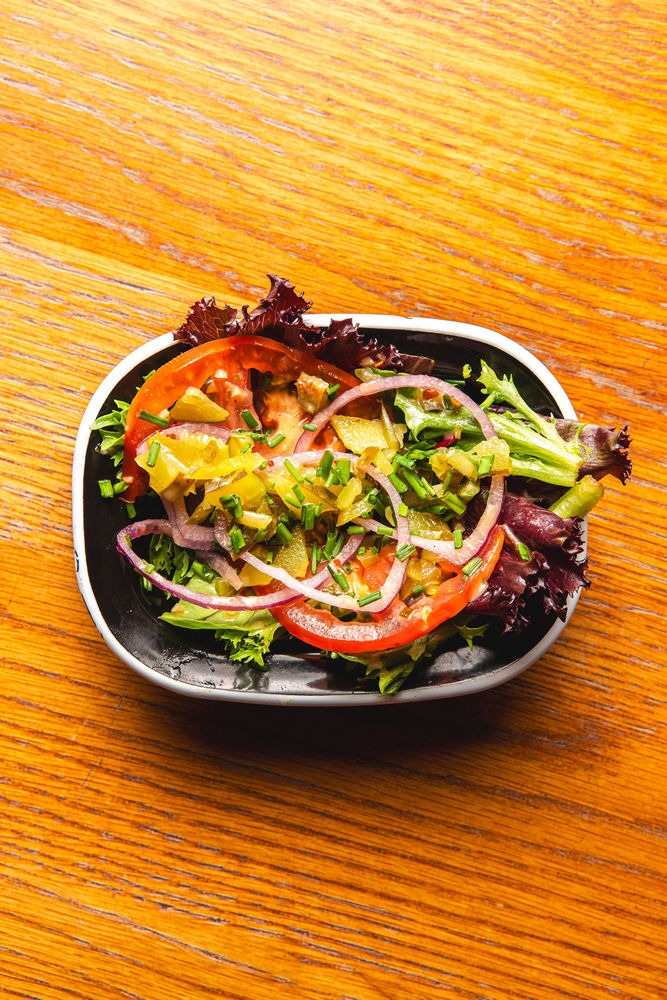This salad features a delightful mix of fresh mixed greens, ripe tomatoes, crunchy red onions, and tangy pickles.