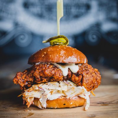A ho0t n spicy Chicken Burger with Blue Cheese Mayo, Fennel, Apple & Blue Cheese Slaw, Gherkin on Top and Sprinkle of Tubby Toms Nashville Dust